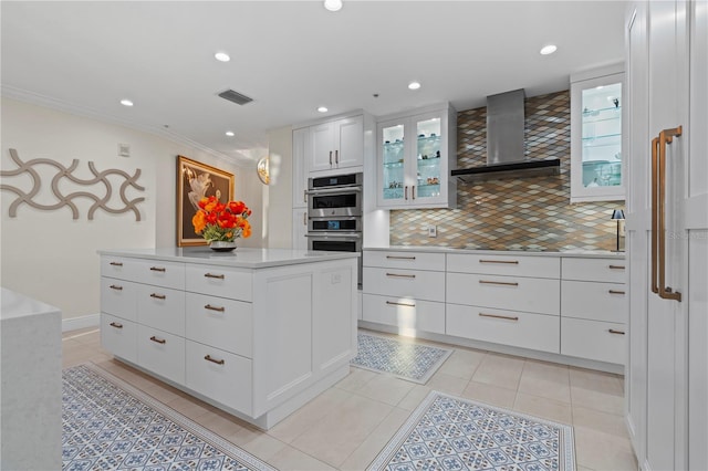 kitchen with white cabinetry, wall chimney exhaust hood, double oven, decorative backsplash, and light tile patterned floors