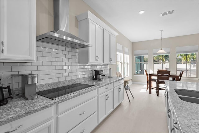 kitchen with wall chimney exhaust hood, backsplash, pendant lighting, black electric cooktop, and white cabinets