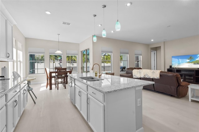 kitchen featuring light stone countertops, sink, pendant lighting, a center island with sink, and white cabinets