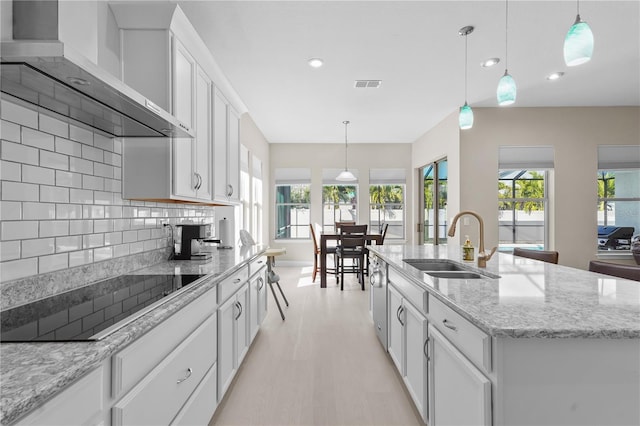 kitchen featuring black electric stovetop, tasteful backsplash, a kitchen island with sink, sink, and white cabinetry