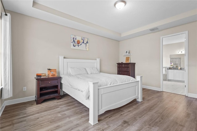 bedroom with a raised ceiling, ensuite bathroom, and light hardwood / wood-style flooring