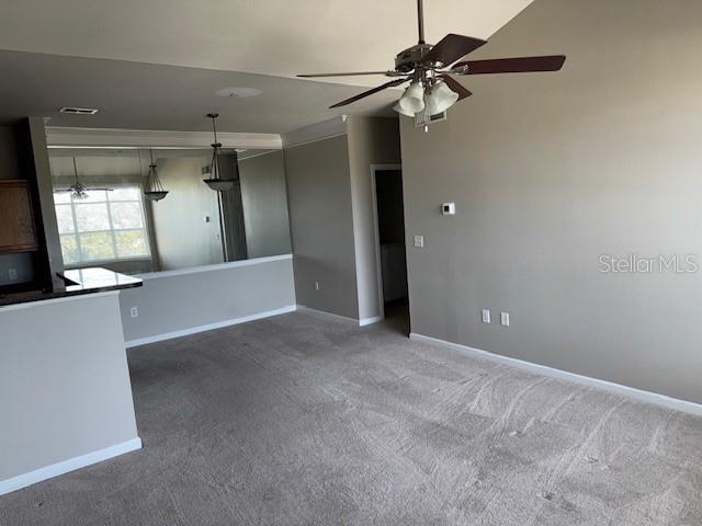 unfurnished living room featuring dark carpet, ceiling fan, and ornamental molding