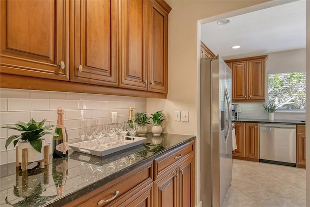 kitchen with light tile patterned flooring, appliances with stainless steel finishes, backsplash, and dark stone countertops