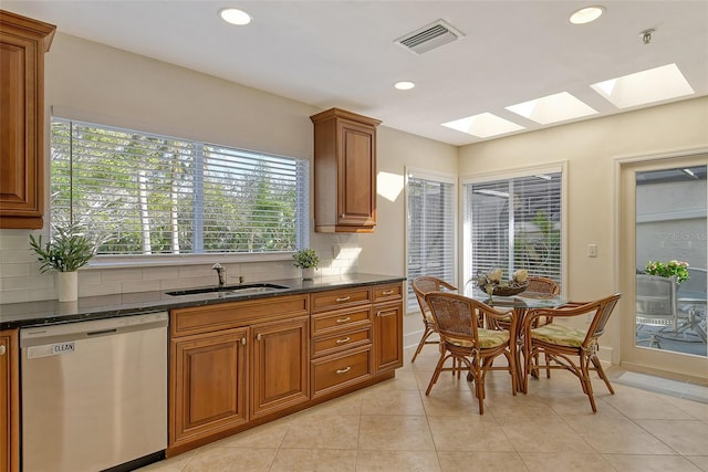 kitchen featuring sink, dark stone countertops, backsplash, stainless steel dishwasher, and light tile patterned floors