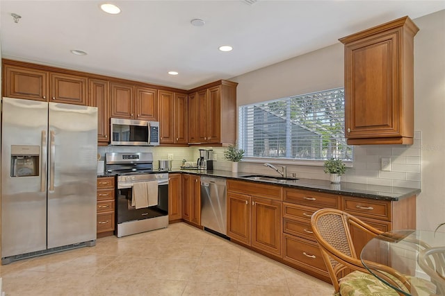 kitchen with sink, decorative backsplash, dark stone counters, light tile patterned floors, and stainless steel appliances