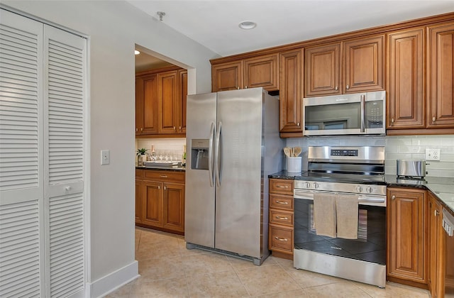 kitchen with light tile patterned floors, decorative backsplash, dark stone counters, and appliances with stainless steel finishes