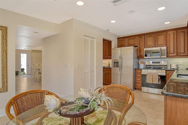 kitchen with light tile patterned flooring, stainless steel appliances, tasteful backsplash, and dark stone countertops