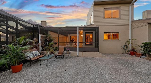 back house at dusk featuring a lanai and a patio