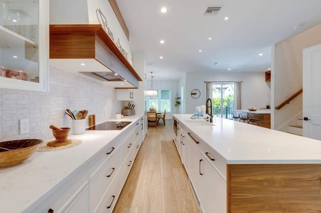 kitchen with sink, white cabinetry, a large island with sink, black electric cooktop, and light hardwood / wood-style floors