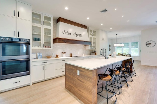 kitchen with sink, tasteful backsplash, an island with sink, white cabinets, and stainless steel double oven