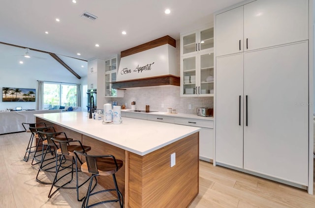 kitchen with a breakfast bar area, a large island with sink, white cabinets, light hardwood / wood-style floors, and backsplash