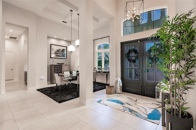 tiled foyer featuring a notable chandelier, french doors, a high ceiling, and coffered ceiling