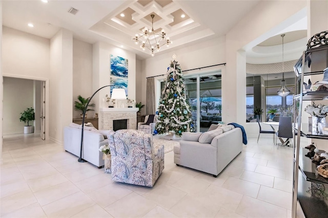 tiled living room featuring coffered ceiling, a high ceiling, a raised ceiling, a stone fireplace, and a chandelier