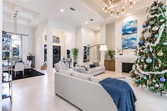 living room featuring coffered ceiling, a high ceiling, a stone fireplace, a chandelier, and light tile patterned flooring