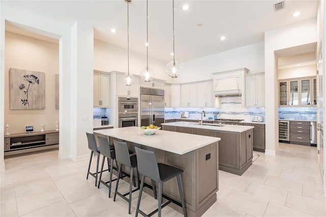 kitchen with a kitchen bar, premium range hood, stainless steel appliances, a kitchen island with sink, and decorative light fixtures