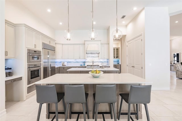 kitchen featuring a kitchen island with sink, hanging light fixtures, light tile patterned flooring, and stainless steel appliances