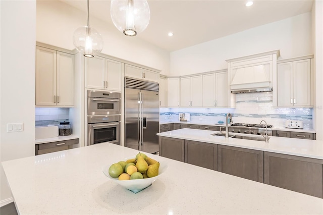 kitchen featuring appliances with stainless steel finishes, tasteful backsplash, premium range hood, sink, and decorative light fixtures