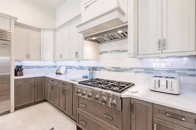 kitchen featuring decorative backsplash, light stone countertops, custom range hood, stainless steel appliances, and light tile patterned floors