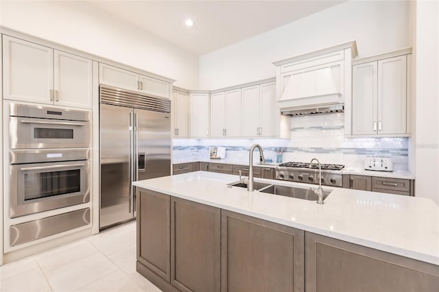 kitchen with light stone countertops, tasteful backsplash, premium range hood, stainless steel appliances, and sink