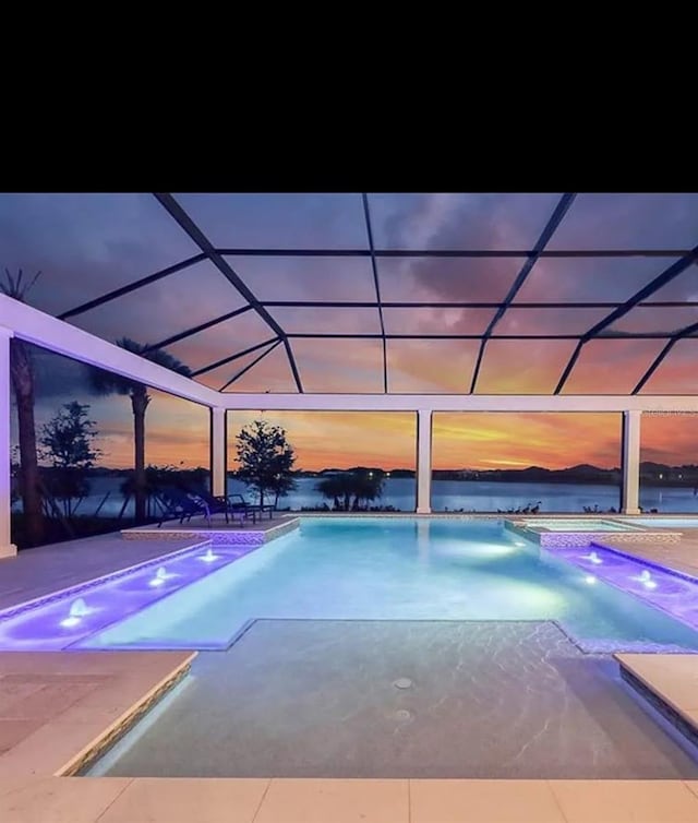 pool at dusk featuring glass enclosure and a patio