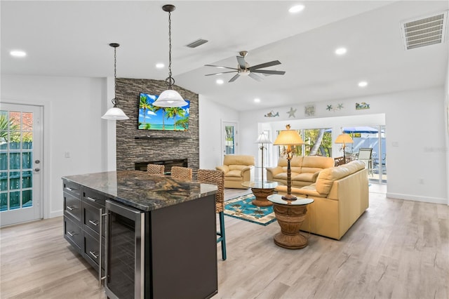 kitchen with light wood-type flooring, a stone fireplace, beverage cooler, and dark stone countertops