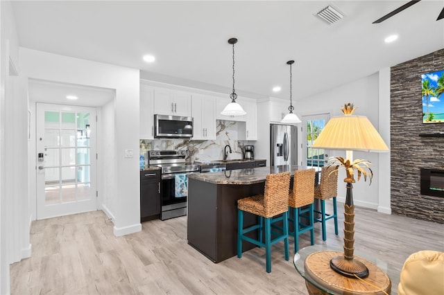 kitchen with appliances with stainless steel finishes, vaulted ceiling, dark stone countertops, white cabinets, and a kitchen island