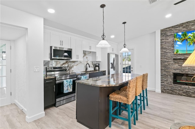 kitchen featuring a kitchen breakfast bar, dark stone counters, stainless steel appliances, a kitchen island, and white cabinetry