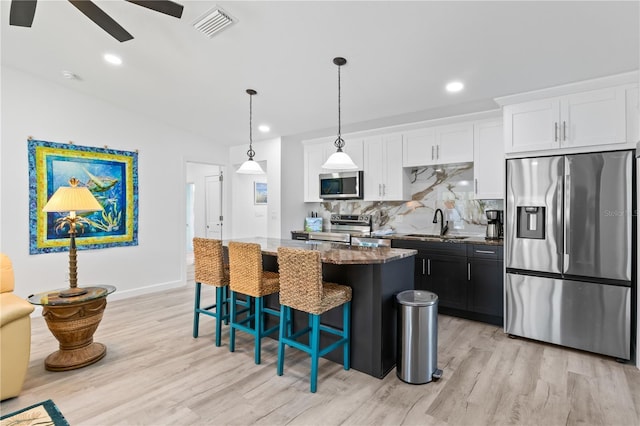 kitchen featuring light wood-type flooring, stainless steel appliances, a center island, white cabinetry, and hanging light fixtures