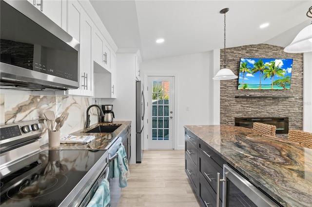 kitchen with appliances with stainless steel finishes, vaulted ceiling, beverage cooler, pendant lighting, and white cabinetry