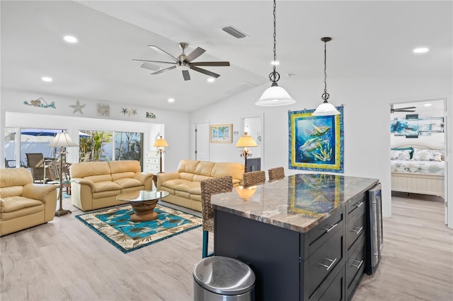 kitchen with vaulted ceiling, ceiling fan, decorative light fixtures, stone counters, and light hardwood / wood-style floors