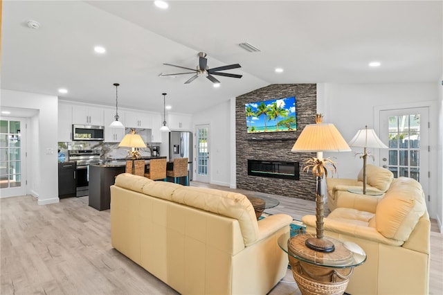 living room featuring a fireplace, light hardwood / wood-style floors, vaulted ceiling, and ceiling fan