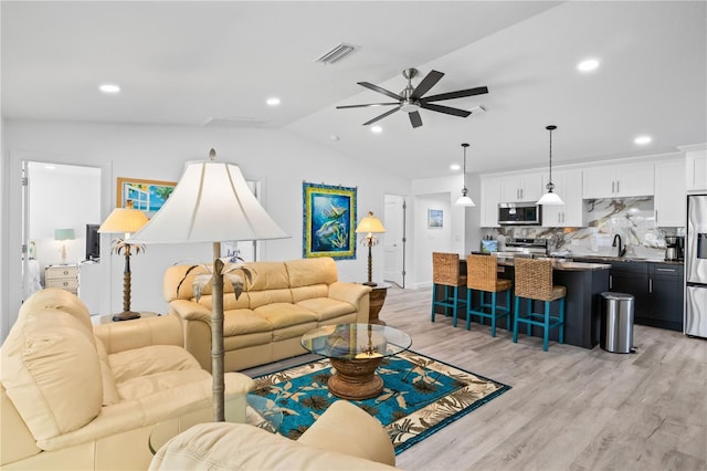 living room with ceiling fan, sink, lofted ceiling, and light wood-type flooring