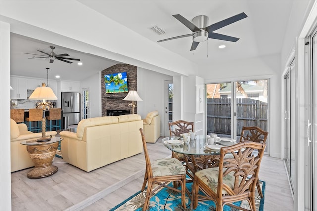 dining area with a brick fireplace, ceiling fan, and light hardwood / wood-style flooring