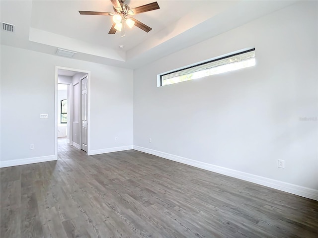 empty room featuring a raised ceiling, ceiling fan, and dark wood-type flooring