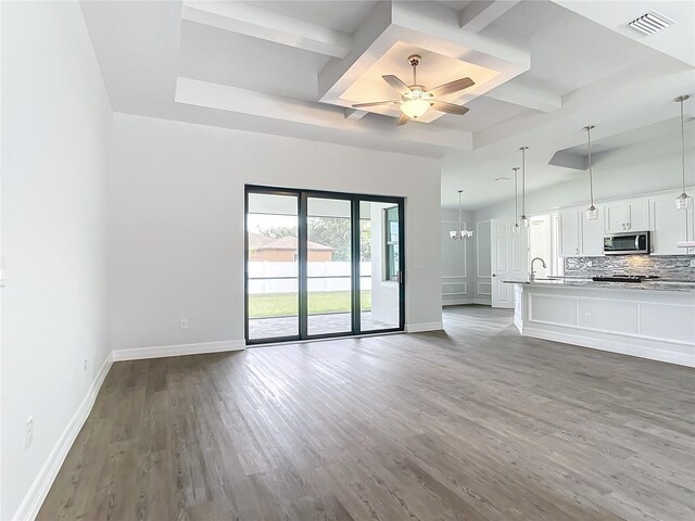 unfurnished living room featuring a tray ceiling, sink, wood-type flooring, and ceiling fan with notable chandelier