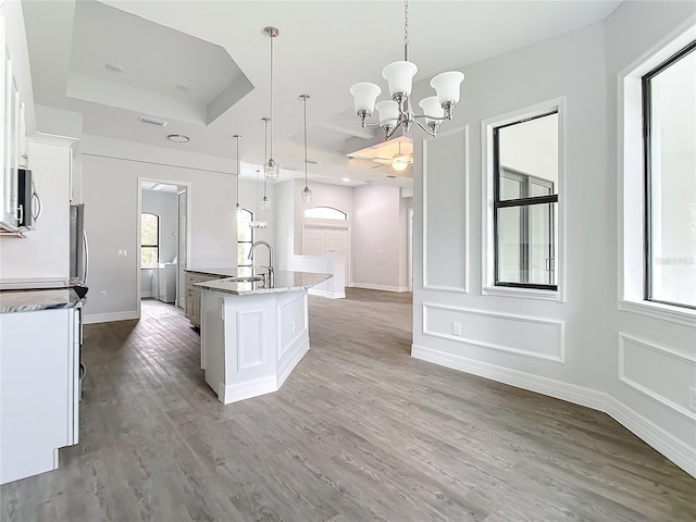 kitchen featuring white cabinets, a kitchen island with sink, hanging light fixtures, and a tray ceiling