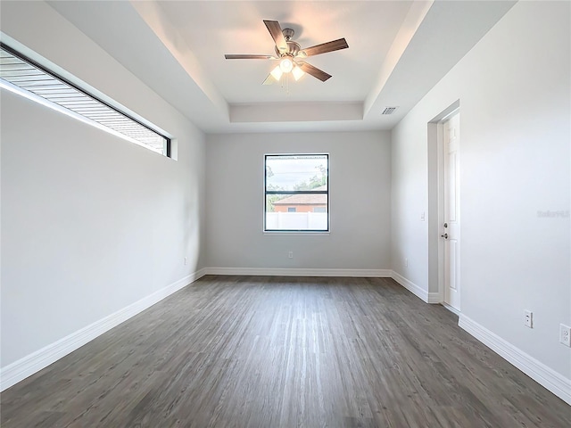 spare room featuring a tray ceiling, ceiling fan, and dark wood-type flooring