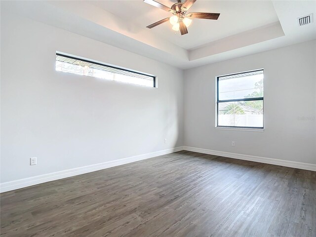 empty room with ceiling fan, a raised ceiling, and dark wood-type flooring