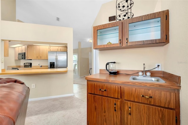 kitchen featuring lofted ceiling, sink, light colored carpet, kitchen peninsula, and stainless steel appliances