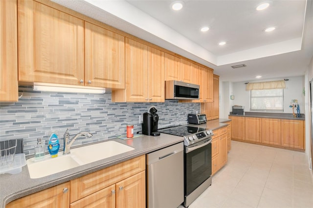 kitchen featuring light brown cabinets, backsplash, sink, a tray ceiling, and stainless steel appliances