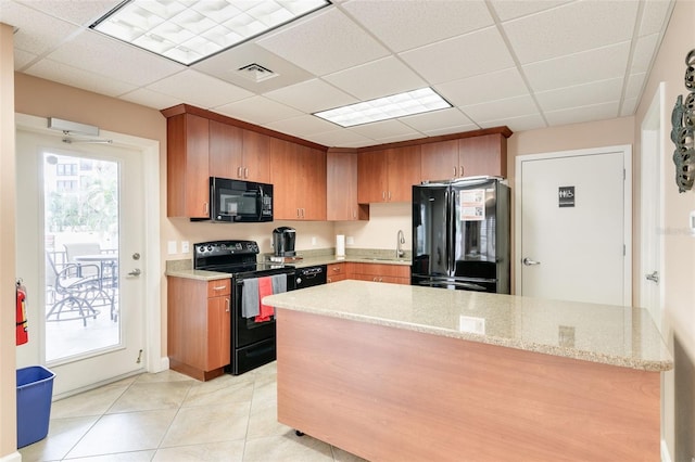 kitchen featuring black appliances, a drop ceiling, light stone counters, and sink