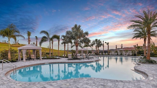 pool at dusk with a gazebo and a patio area