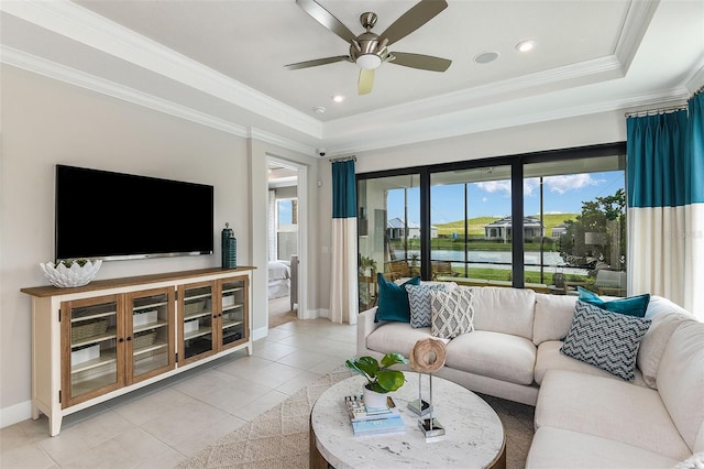 tiled living room with a raised ceiling, ceiling fan, a water view, and ornamental molding