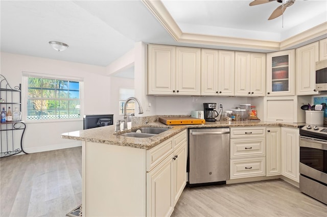 kitchen with light stone countertops, sink, kitchen peninsula, a tray ceiling, and appliances with stainless steel finishes