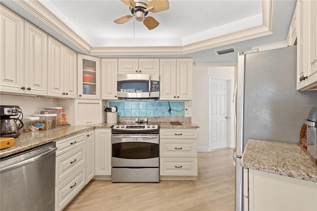 kitchen featuring light stone countertops, appliances with stainless steel finishes, light wood-type flooring, and a tray ceiling