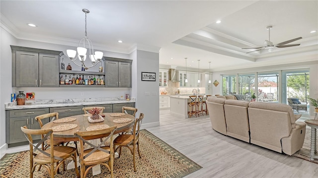 dining area with sink, crown molding, light hardwood / wood-style floors, a tray ceiling, and ceiling fan with notable chandelier