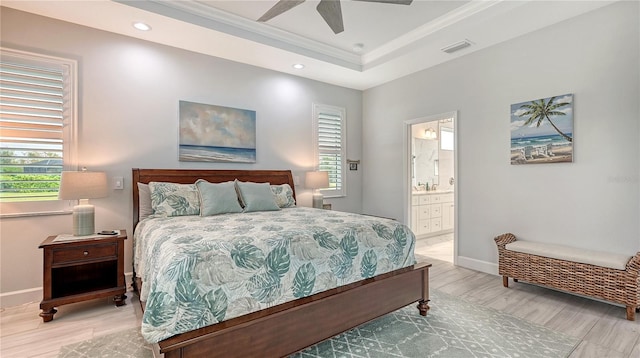 bedroom featuring connected bathroom, ceiling fan, a raised ceiling, crown molding, and light wood-type flooring