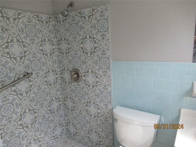 bathroom featuring tiled shower, vanity, toilet, and tile walls