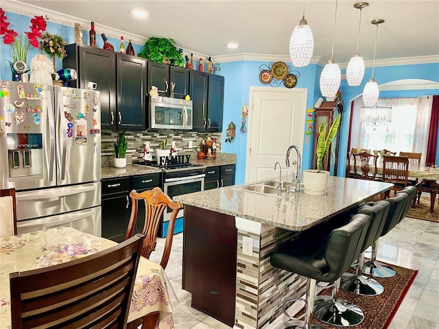 kitchen featuring pendant lighting, sink, light stone countertops, an island with sink, and stainless steel appliances