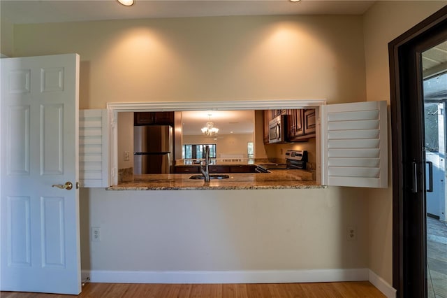 kitchen with kitchen peninsula, light wood-type flooring, stainless steel appliances, stone counters, and a chandelier